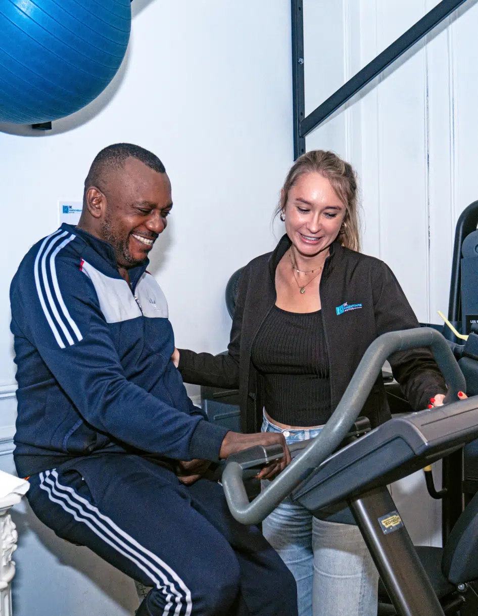 Homme suivant une séance de rééducation sur vélo stationnaire avec un thérapeute | Ik Paris