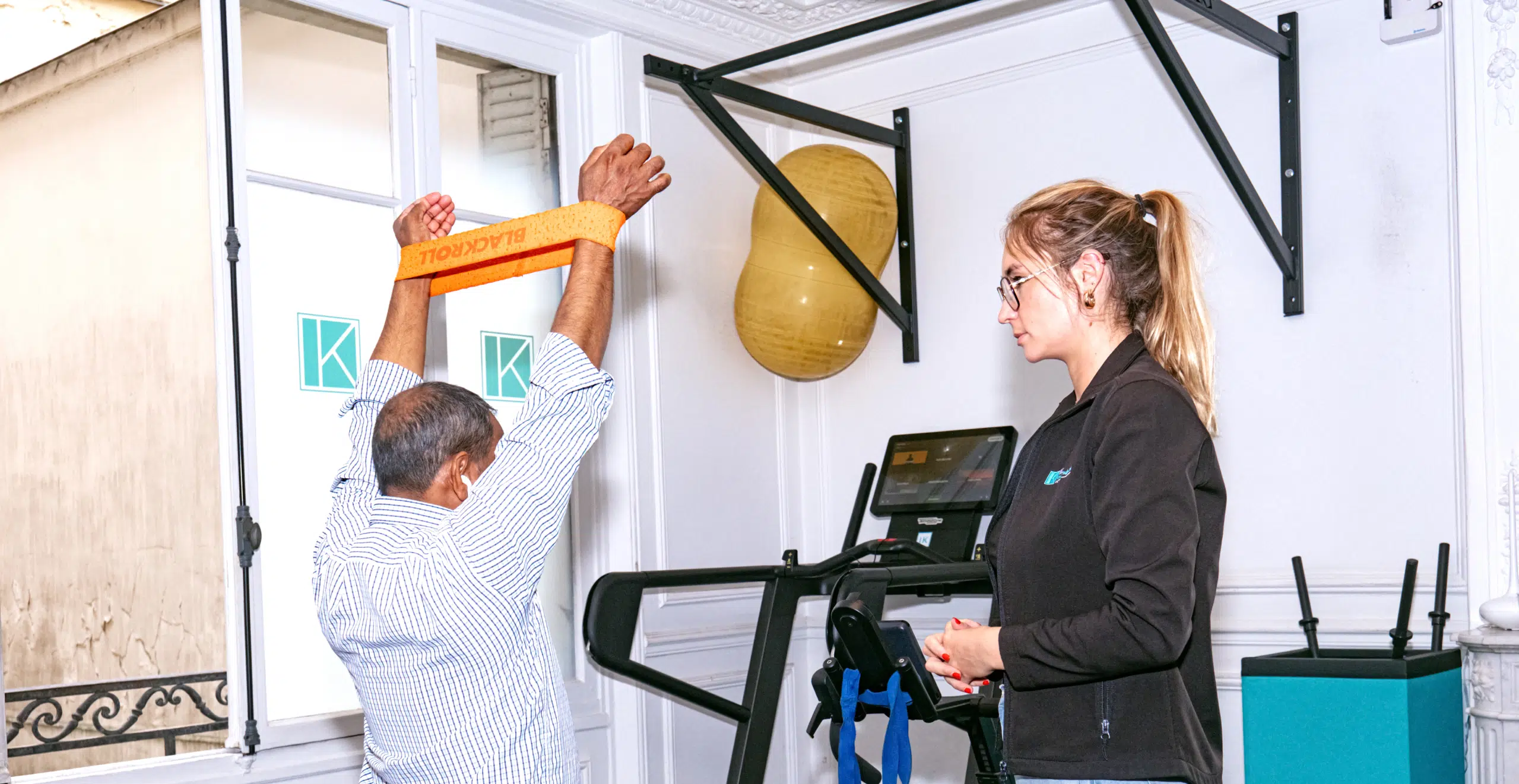 Homme âgé effectuant un exercice debout avec un élastique- Pathologie acromio-claviculaire | Ik Paris